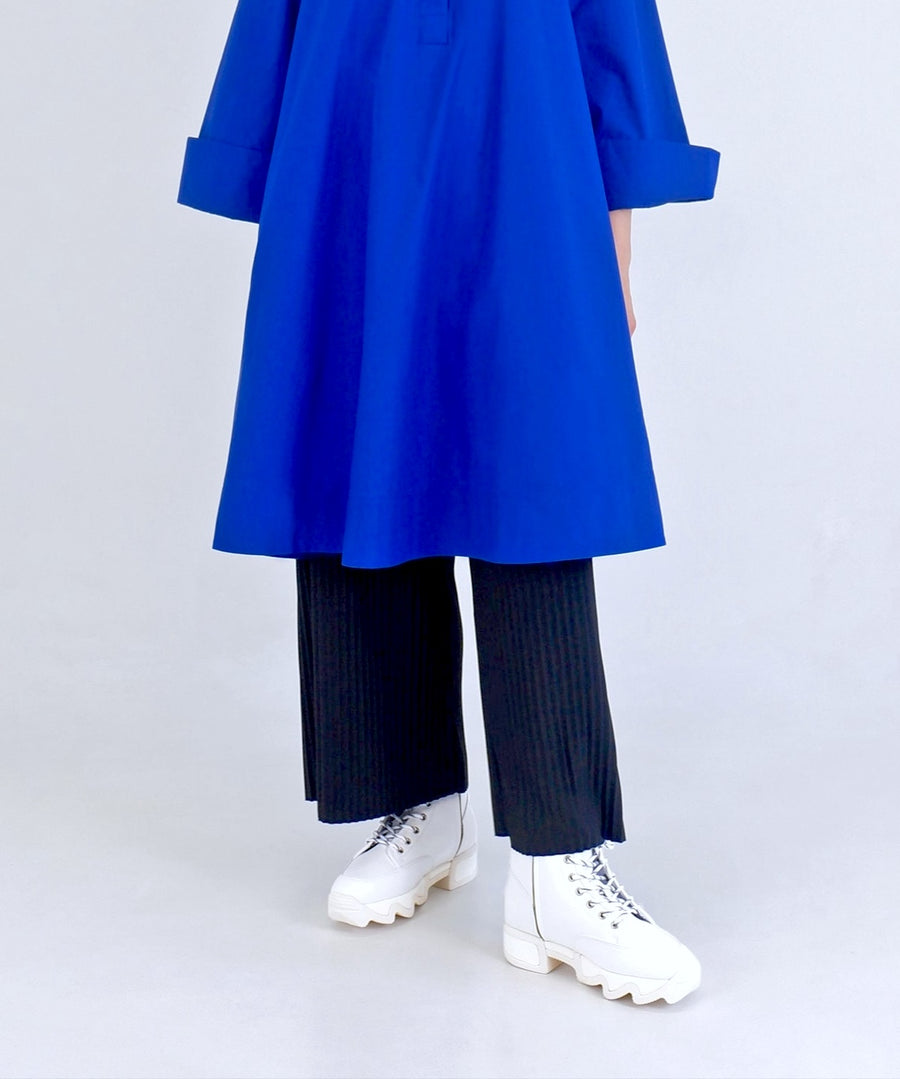 Person wearing a blue coat, dark pants, and white boots on a light gray background
