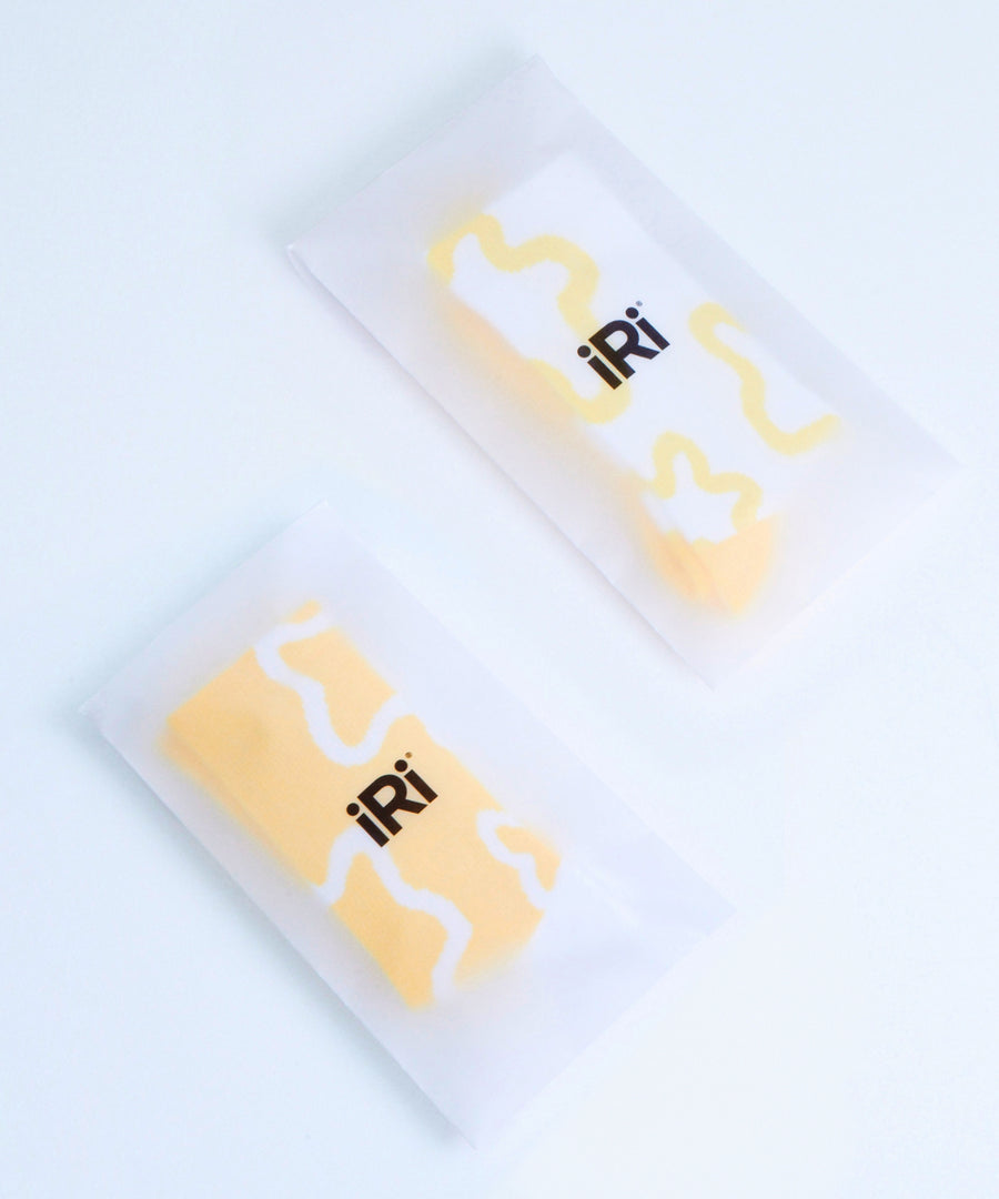 Yellow and white socks with iRi iconic abstract patterns on a pale grey background, inside iRi branded paper pacakging