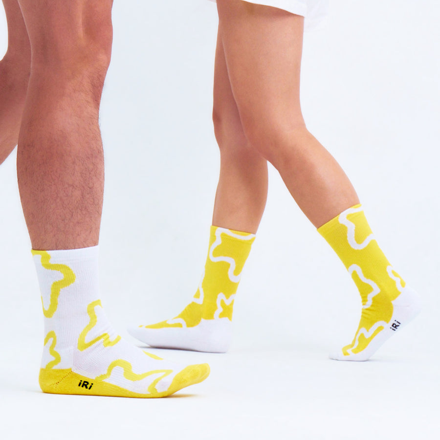 Yellow and white socks with iRi iconic abstract patterns worn on male and female models on a pale grey background