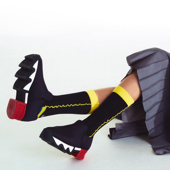 A model wearing black pleated long pants with WES Black Red Low Top Sneaker, styled with knee-length DANCING QUEEN burgundy cotton socks